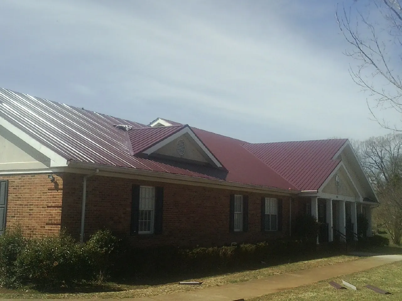 Red metal roof with gabled entries on a long brick building, from a Hail Damage Roof Repair job in Westcliffe