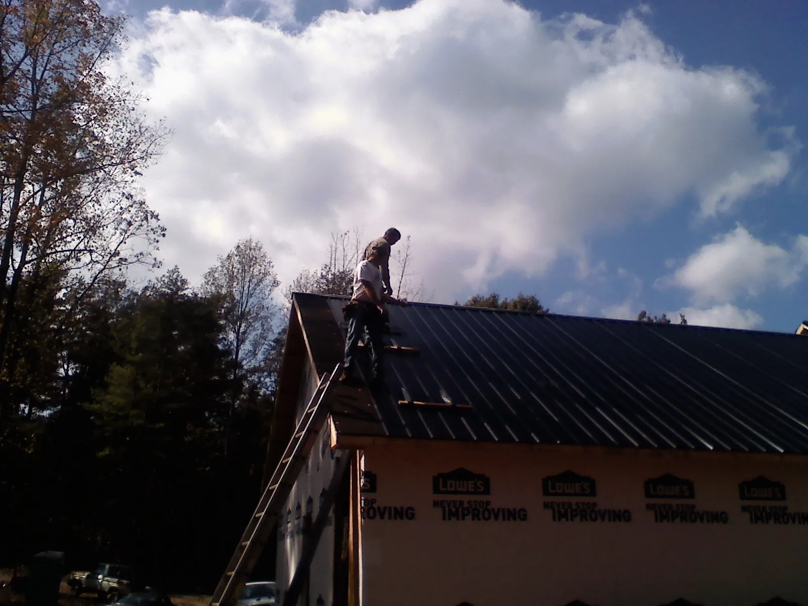 Roofer fastening dark metal panels high against a cloudy sky, from a Roof Inspection job in Westcliffe