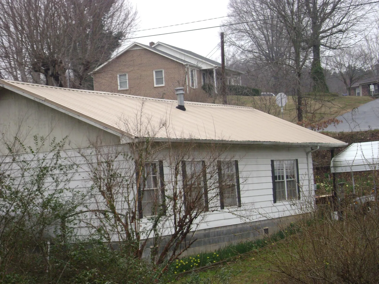 Tan metal roof on a white sided house set into a hillside — Commercial Roofing by Roofing Brothers in Westcliffe